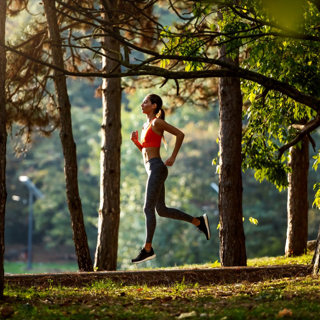 A woman enjoys a nice jog through a sunny forrest.