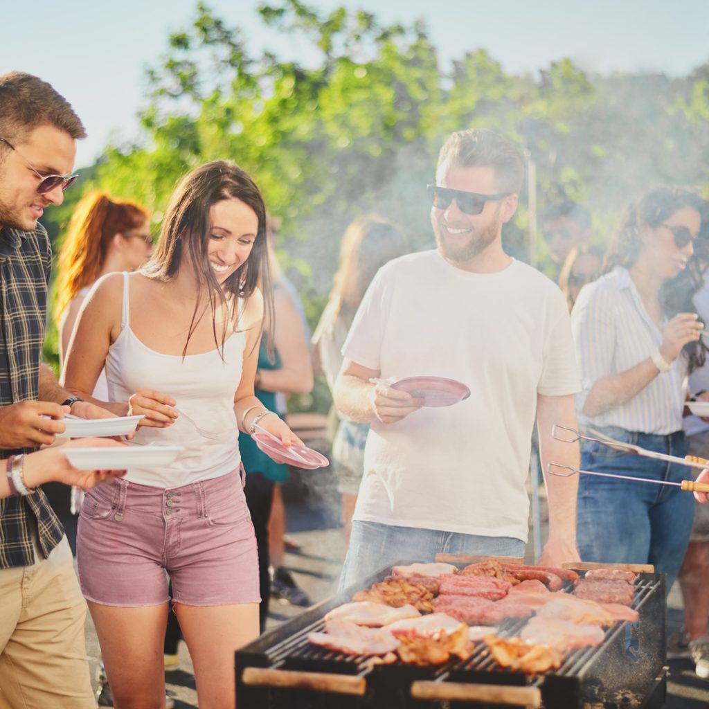 A group of friends stand around the grill during an outdoor Labor Day celebration.