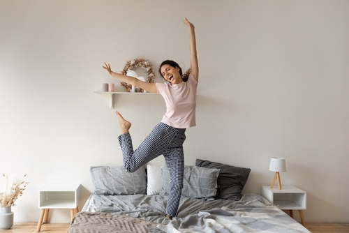 A woman jumps on her bed to celebrate.