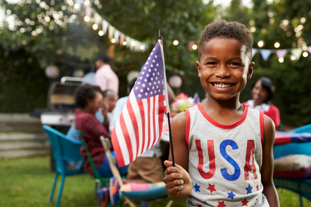 A young American boy proudly holds up a small flag to celebrate the 4th of July.
