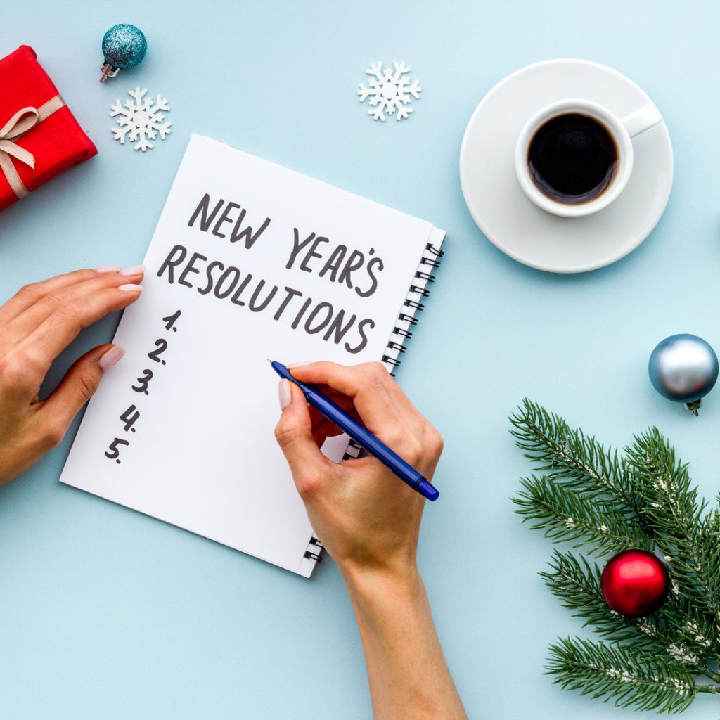 A person sits with pen, paper, and a cup of coffee to write their New Year's Resolutions.
