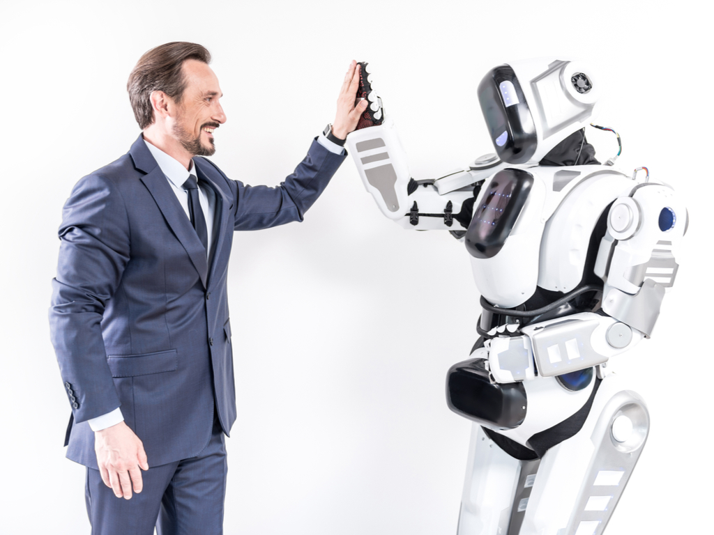 A man gives a friendly greeting to aa robot which represents the BidBuddy tool DealDash provides.
