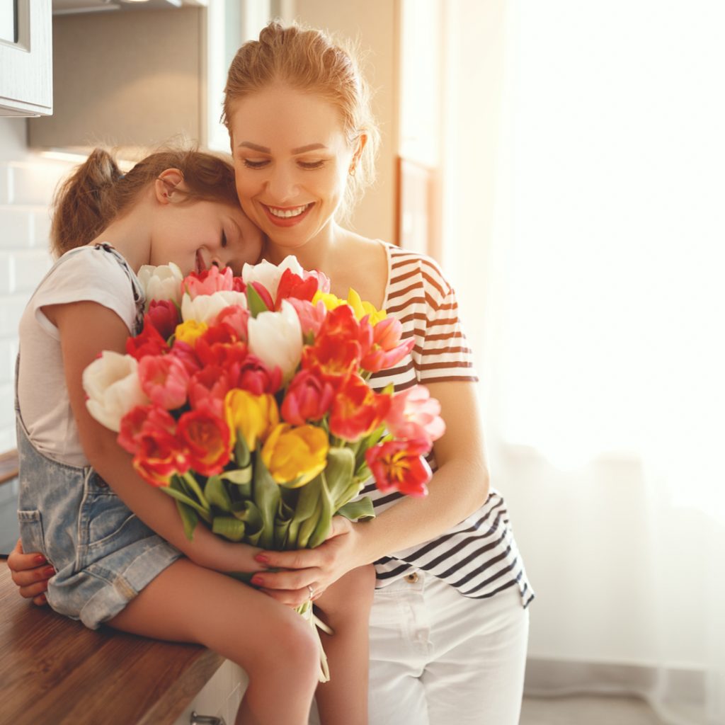 A mother and daughter embrace while enjoying a bouquet of tulips on Mother's Day.