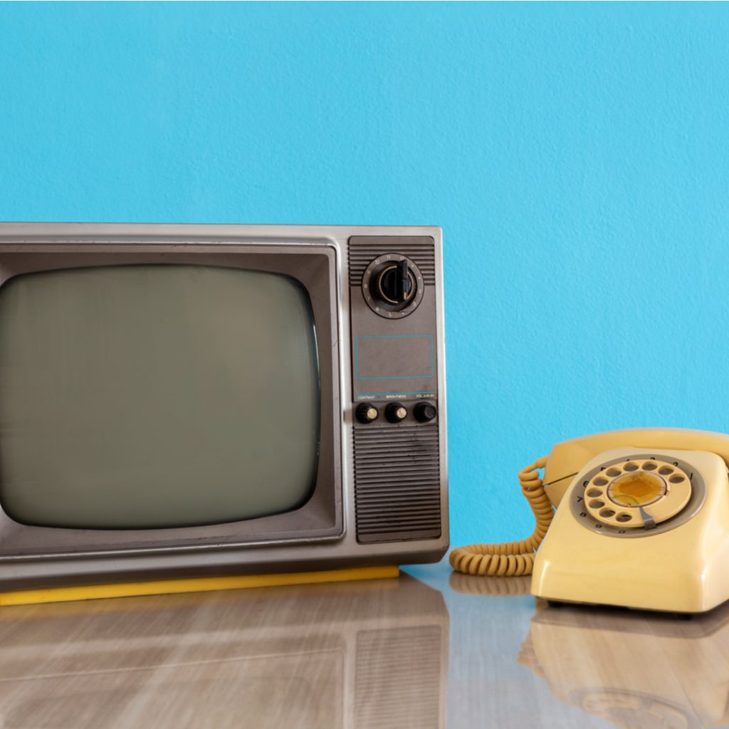 A vintage TV and telephone sit on a wooden table.