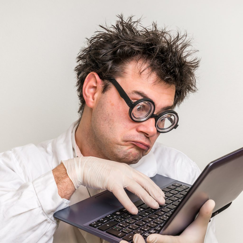 A disheveled scientist holds up a laptop as he frantically works on his latest creation.