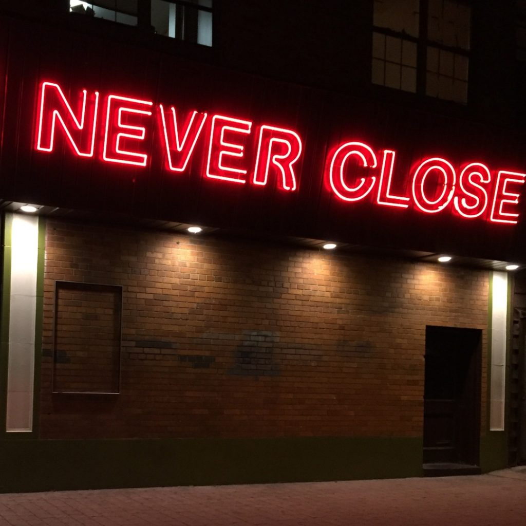 A neon that reads, 'never close' indicates that a business is always open.