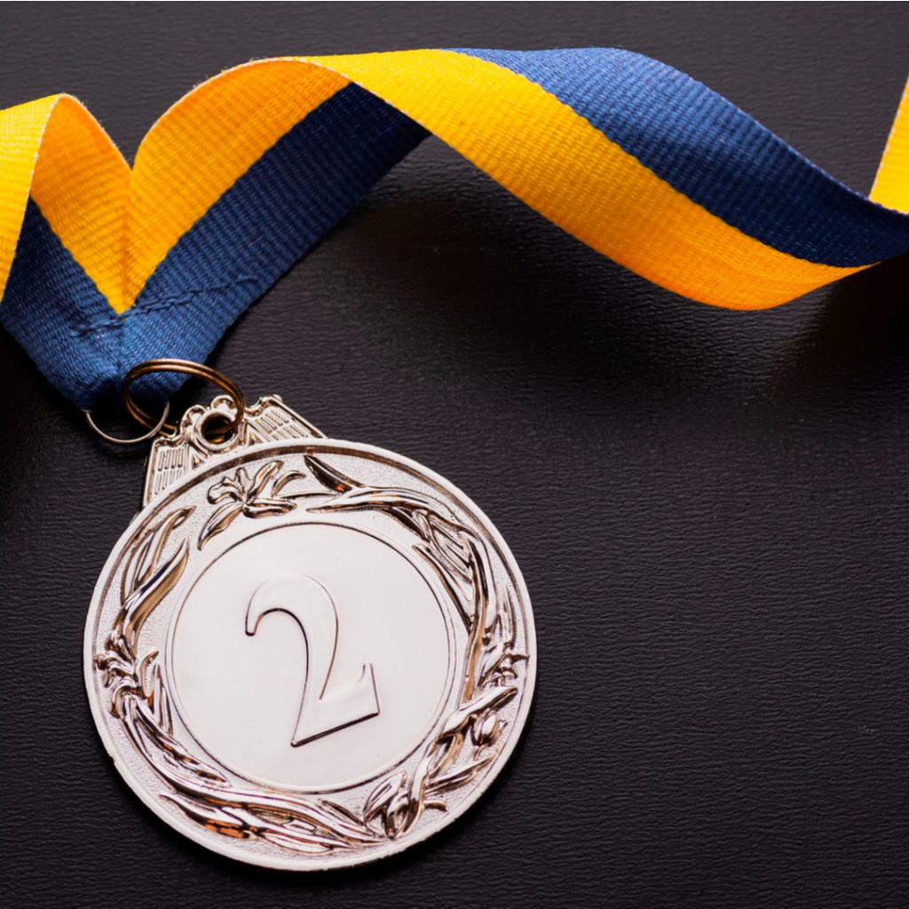 A silver medal attached to a colorful ribbon lies on a table and is  a handsome reward for finishing second.