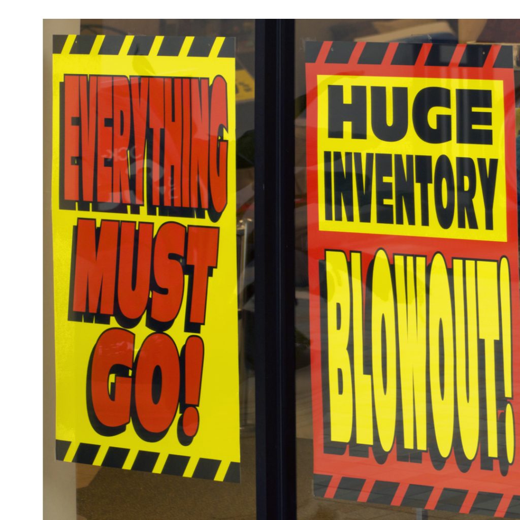 Signs in a store window advertise a sales event where everything must go.