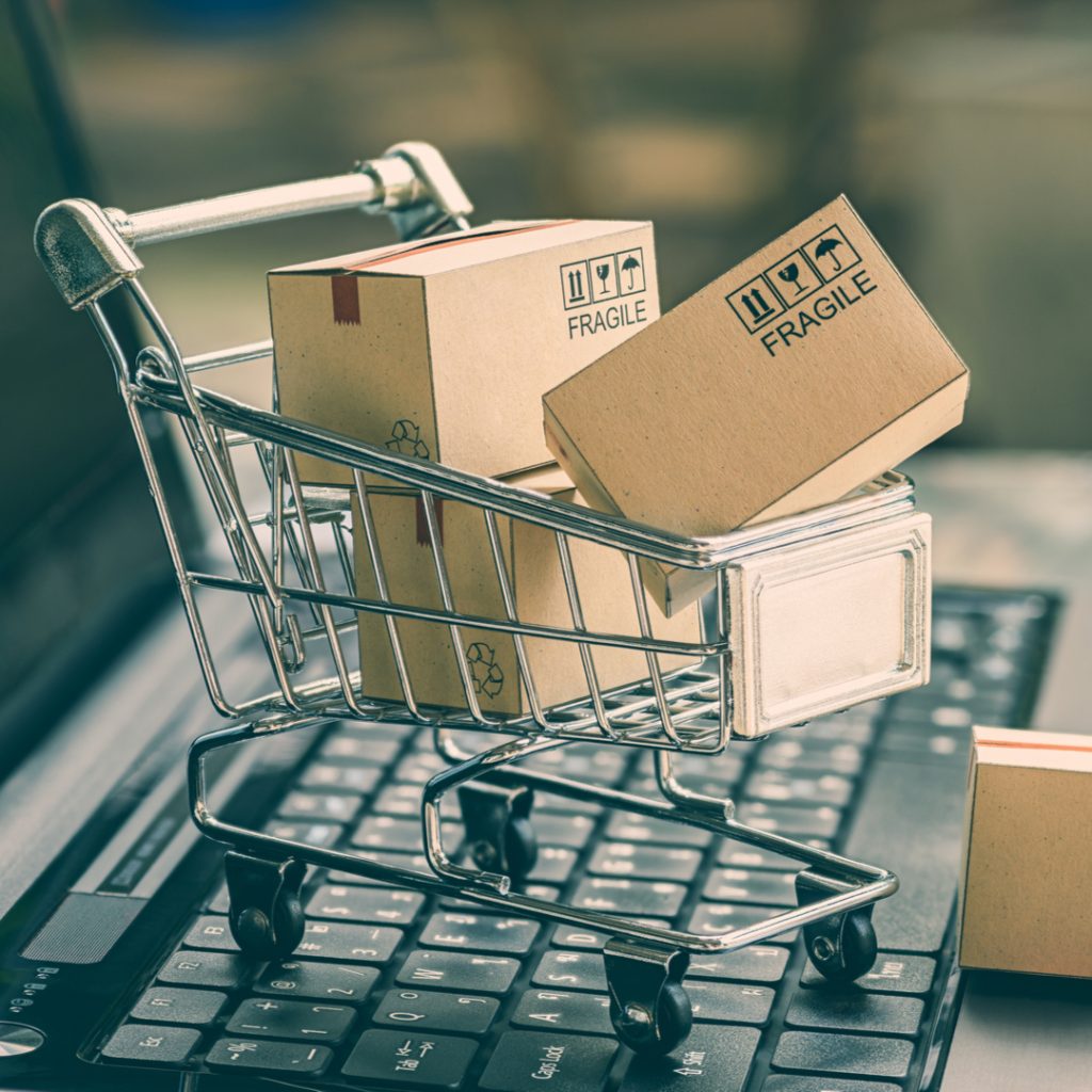 A small shopping cart full or packages sits atop a laptop keyboard to illustrate the power of online shopping.
