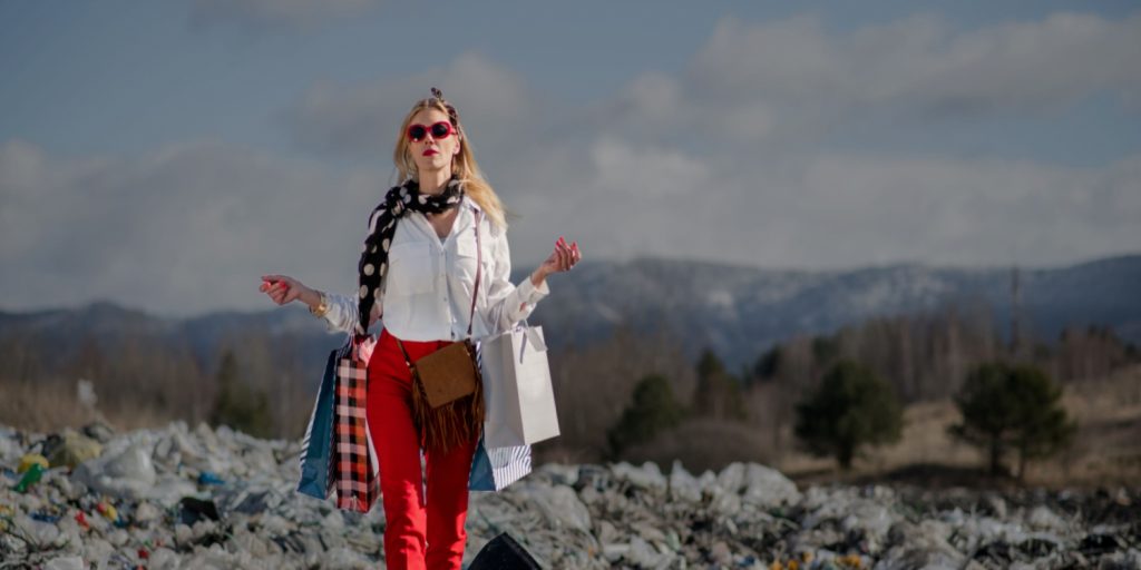 A fashionable women wearing expensive clothes walks through a landfill.